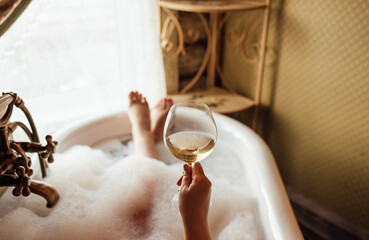 Close-up of a hand holding an elegant glass of champagne in the bathroom. A young woman takes a...