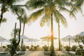 Beachfront with tall palm trees and lounge chairs under white umbrellas at sunset