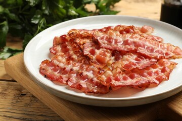 Plate with fried bacon slices on wooden table, closeup