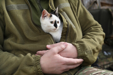 Soldier in uniform warming little stray cat, closeup