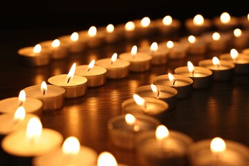 Burning candles on wooden table in darkness, closeup