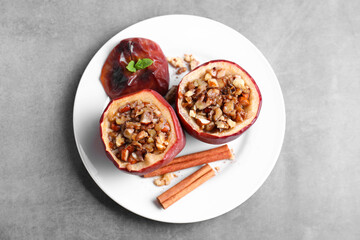 Tasty baked apples with nuts, honey, cinnamon sticks and mint on gray table, top view