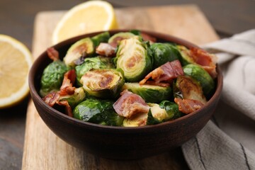 Delicious roasted Brussels sprouts and bacon in bowl on table, closeup