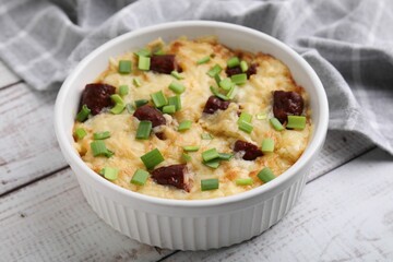 Tasty sausage casserole with green onion in baking dish on white wooden table, closeup