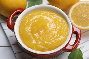 Delicious lemon curd in bowl and fresh citrus fruits on table, closeup