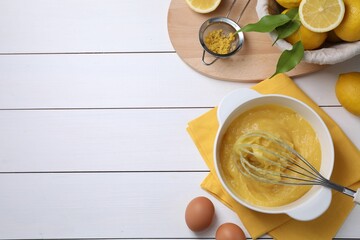 Delicious lemon curd in bowl, ingredients, whisk and sieve on white wooden table, flat lay. Space...