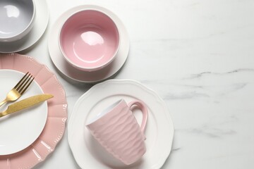 Beautiful ceramic dishware, cutlery and cup on white marble table, flat lay. Space for text