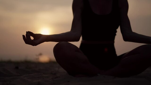 Female practices yoga on ocean at sunset. Close up sporty yoga woman doing yoga pose asana exercise meditation at sunset on beach in nature close up. Health, morning routine, and relax concept.
