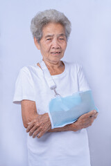 Close-up portrait of an 80s-year-old Senior woman with broken arm and wearing a sling isolated on a...