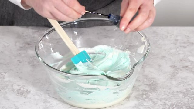 Mixing in blue food coloring into the buttercream frosting.