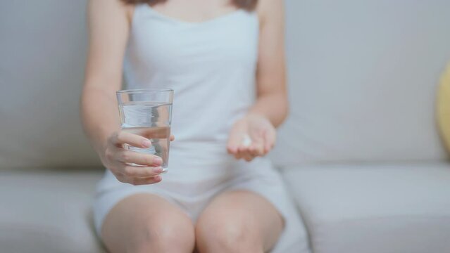 woman hand holding medicine painkiller pill and water glass on the sofa at home, taking for headaches, stomach ache, Diarrhea Pain from food poisoning, Endometriosis, Hysterectomy and Menstrual