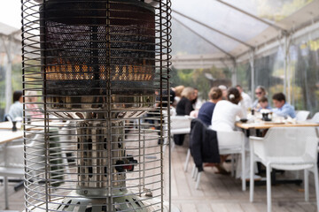 A close-up of the flames of a gas heater, amidst the lively ambiance of an outdoor dining area, where crowds of people gather to enjoy food together, creating a warm and inviting atmosphere.