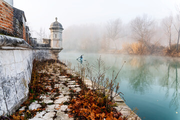 Historic guardhouse, a canoeist and fog at river Tagus in Aranjuez.  Madrid. Spain. Europe.