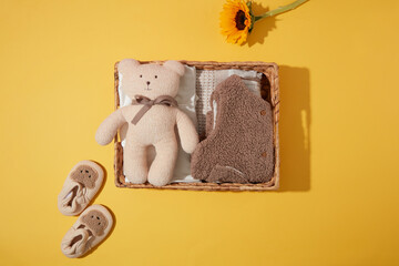 A rattan rectangle basket contains several of baby items, a cute teddy bear, brown feather gilet...