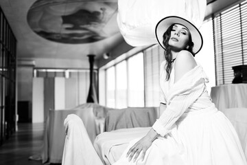 Elegant fashionable woman wearing summer white dress, straw hat, posing in stylish boho interior. - 791548162