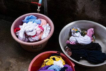A pile of dirty clothes are in a few different bowls. The bowls are pink, yellow, and silver