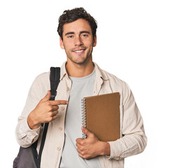 Young Hispanic student with notebook person pointing by hand to a shirt copy space, proud and...