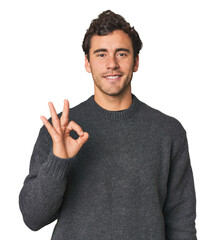 Young Hispanic man in studio cheerful and confident showing ok gesture.
