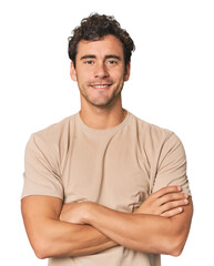 Young Hispanic man in studio who feels confident, crossing arms with determination.