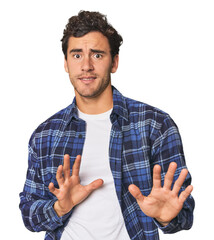 Young Hispanic man in studio rejecting someone showing a gesture of disgust.