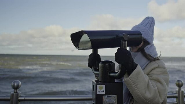 Young girl watches the winter sea through outdoor Binoculars