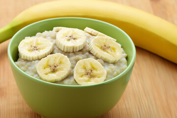 Fototapeta na wymiar porridge with banana. on a wooden table there is a small green plate with milk porridge decorated with banana slices, close-up, useful concept