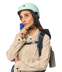 Hispanic young woman with mountain gear looking sideways with doubtful and skeptical expression.
