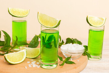 Sweet refreshing mint liqueur, with ice and mint leaves on table background, Shots with lime slice...