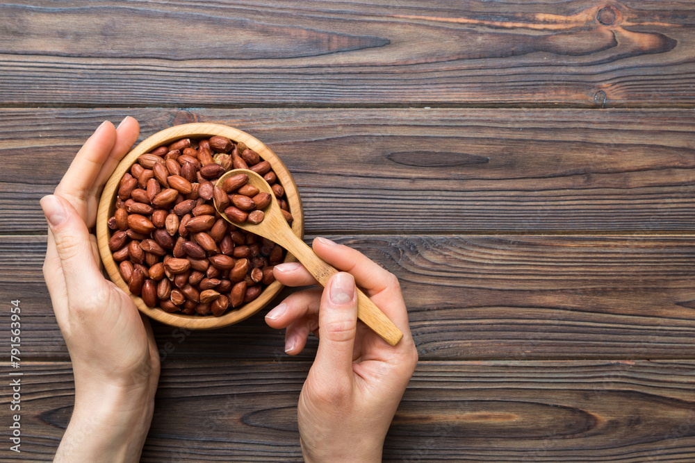 Sticker Woman hands holding a wooden bowl with peanuts. Healthy food and snack. Vegetarian snacks of different nuts