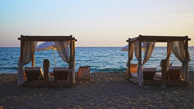 Beach cabana beds and sun loungers on the seashore at sunset.