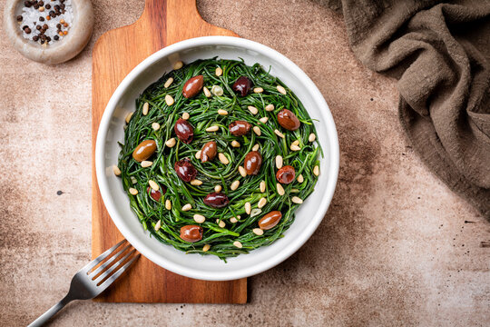 South Italian Salad with Sauteed Agretti or barba di frati with garlic, Taggiasca olives, pinoli or pine nut. Salt, olive oil. Top table view. Brown bacground.
