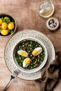 Spring Easter Dinner with Sauteed Agretti with Taggiasca olives, pinoli or pine nut, and boiled eggs. Italian Salad. Boiled spring potato. Top table view, vertical image.