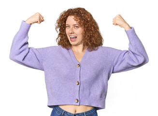 Young Caucasian redhead woman showing strength gesture with arms, symbol of feminine power