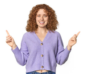 Young Caucasian redhead woman indicates with both fore fingers up showing a blank space.