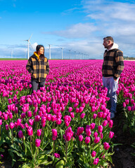 In a vibrant field of purple tulips in the Netherlands, two people stand enchanted by the beauty of Spring, surrounded by windmill turbines