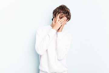 Young caucasian man isolated on blue background blink at the camera through fingers, embarrassed...