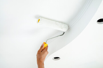 Apartment renovation. A hand with a roller paints the ceiling in white color