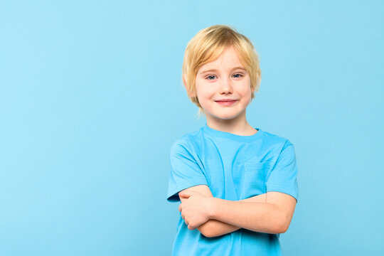 Happy young caucasian boy in casual outfit smiling with arms crossed isolated over pastel blue background.