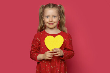 Little girl holding a paper heart on a pink background.
