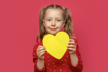Little girl holding a paper heart on a pink background.