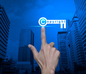 Hand pressing copyright key icon over modern city tower and skyscraper, Copyright and patents concept