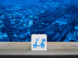 Motorcycle icon on white block cube on wooden table over modern city tower, street, expressway and skyscraper, Business delivery service concept