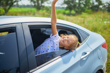 Young Girl Joyfully Waving Hand Out of Car Window on Sunny Day