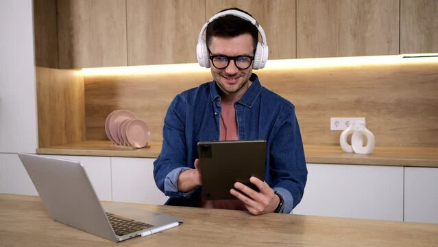 A male student, studying online, uses headphones and a tablet to attend an online education class on the school's video chat platform.
