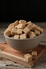 Brown sugar cubes in bowl on wooden table, closeup