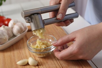 Woman squeezing garlic with press at white table, closeup - obrazy, fototapety, plakaty