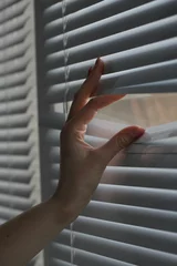 Deurstickers Woman separating slats of white blinds indoors, closeup © New Africa