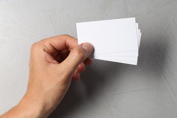 Man holding white blank cards at light grey table, top view. Mockup for design