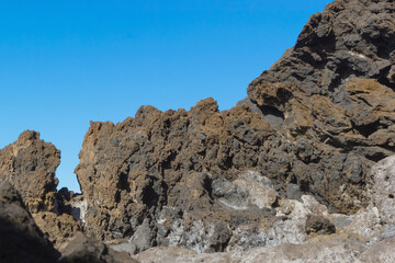 Volcanic rocks of the ocean coast cliff and the blue sky. Black rocky shore. Summer vacations and traveling. Santa Cruz de Tenerife island. Canary islands, Spain - obrazy, fototapety, plakaty
