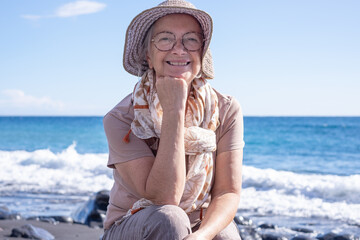 Portrait of Smiling senior Caucasian woman on seaside vacation looking at camera while waves crash...
